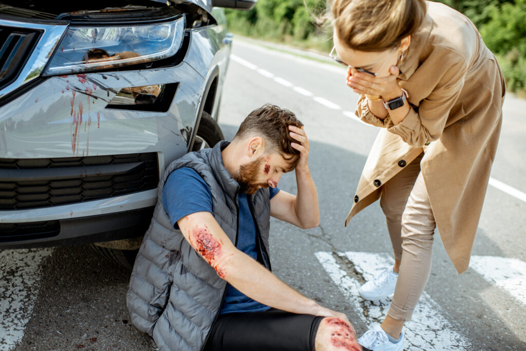 Woman driver feeling sorry about injured man suffering on the pedestrian crossing near the car after the road accident